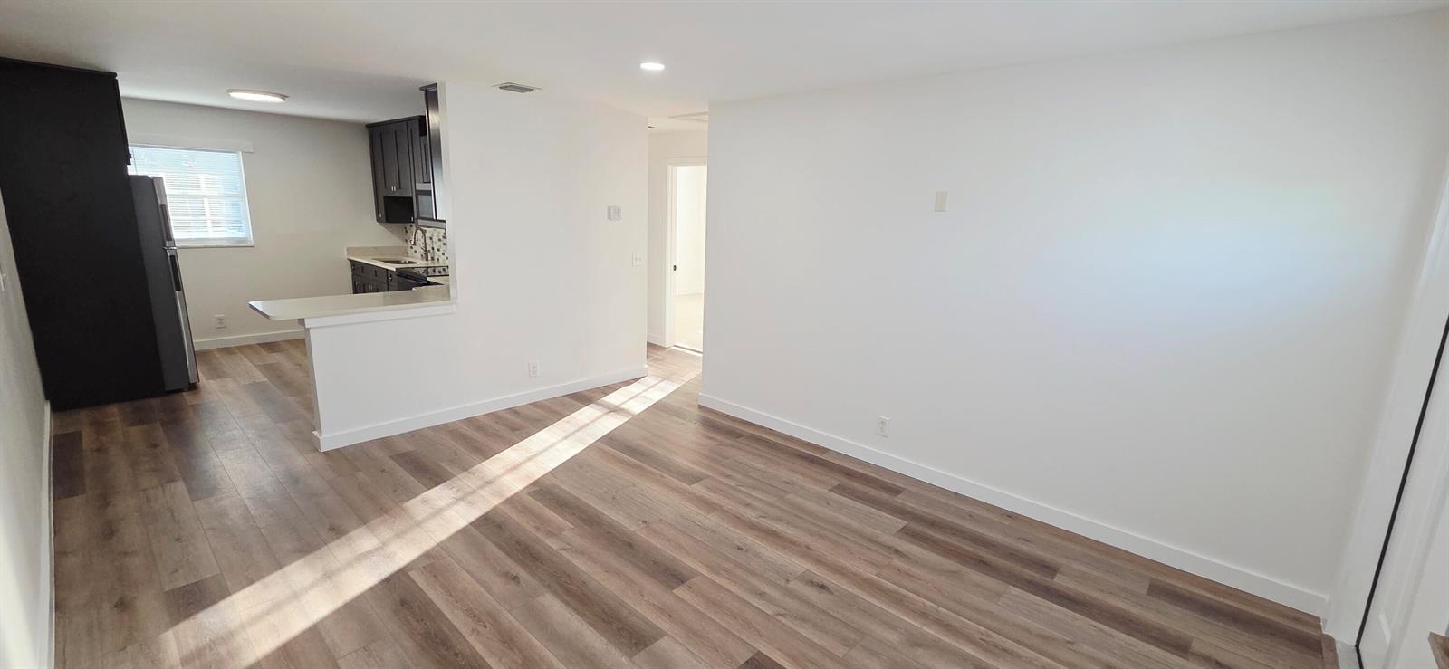 A bright living room with wood-look flooring opens to a kitchen with dark cabinetry — 765 W 7th Street # B, Riviera Beach FL 33404, RIVIERA BEACH, FL