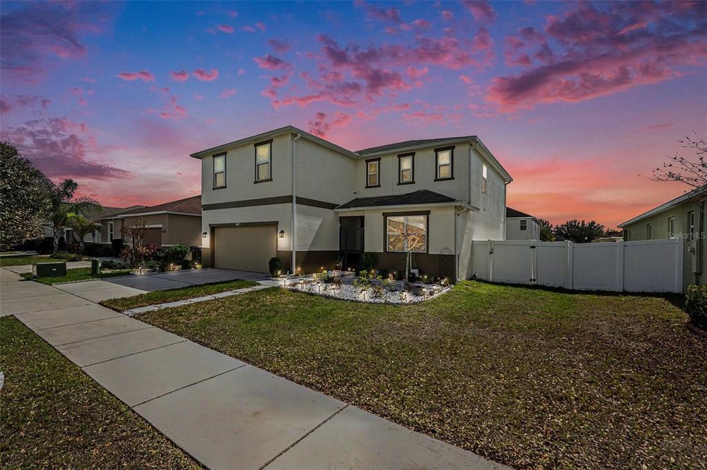 A two-story suburban house with a tan exterior, a two-car garage, and a white fence — 10617 ALDO MORO DRIVE, WIMAUMA, FL