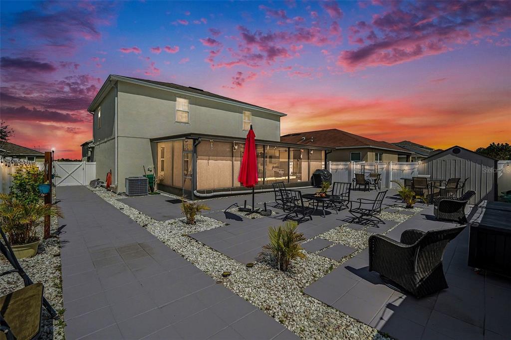 A backyard patio features a screened-in porch, paved walkways, gravel landscaping, and outdoor furniture — 10617 ALDO MORO DRIVE, WIMAUMA, FL