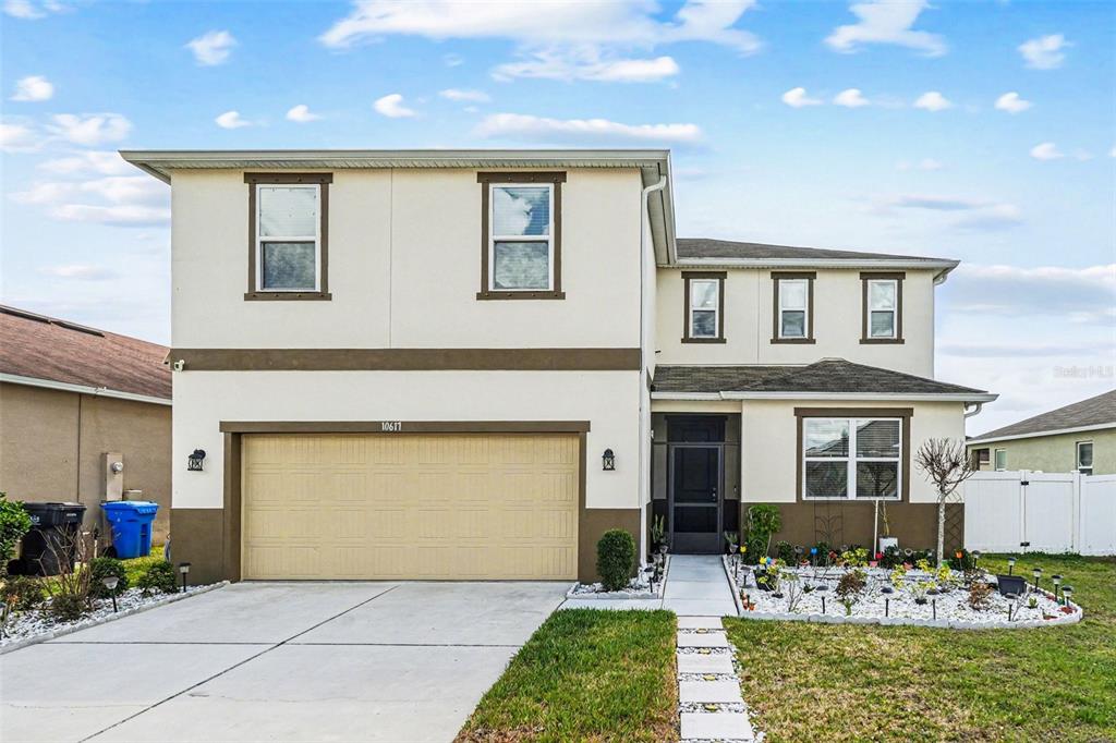 A two-story house with a beige stucco exterior, a two-car garage, and a front walkway — 10617 ALDO MORO DRIVE, WIMAUMA, FL
