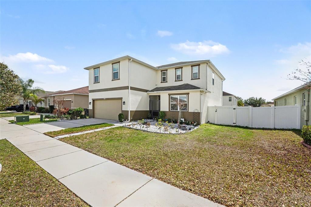 A two-story suburban house with a tan stucco exterior, a two-car garage, and a white fence — 10617 ALDO MORO DRIVE, WIMAUMA, FL