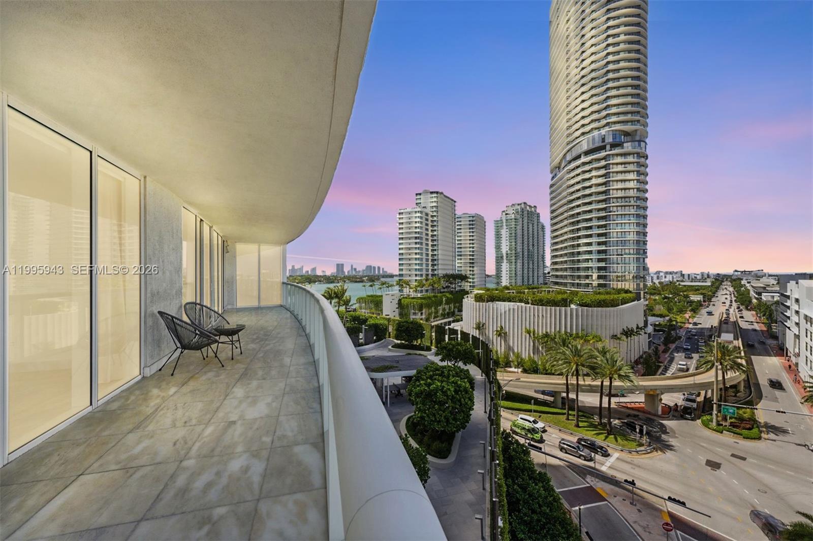 A balcony with two chairs overlooks a city street, lush greenery, and tall residential towers — 450 Alton Rd # 910, Miami Beach FL 33139, MIAMI BEACH, FL