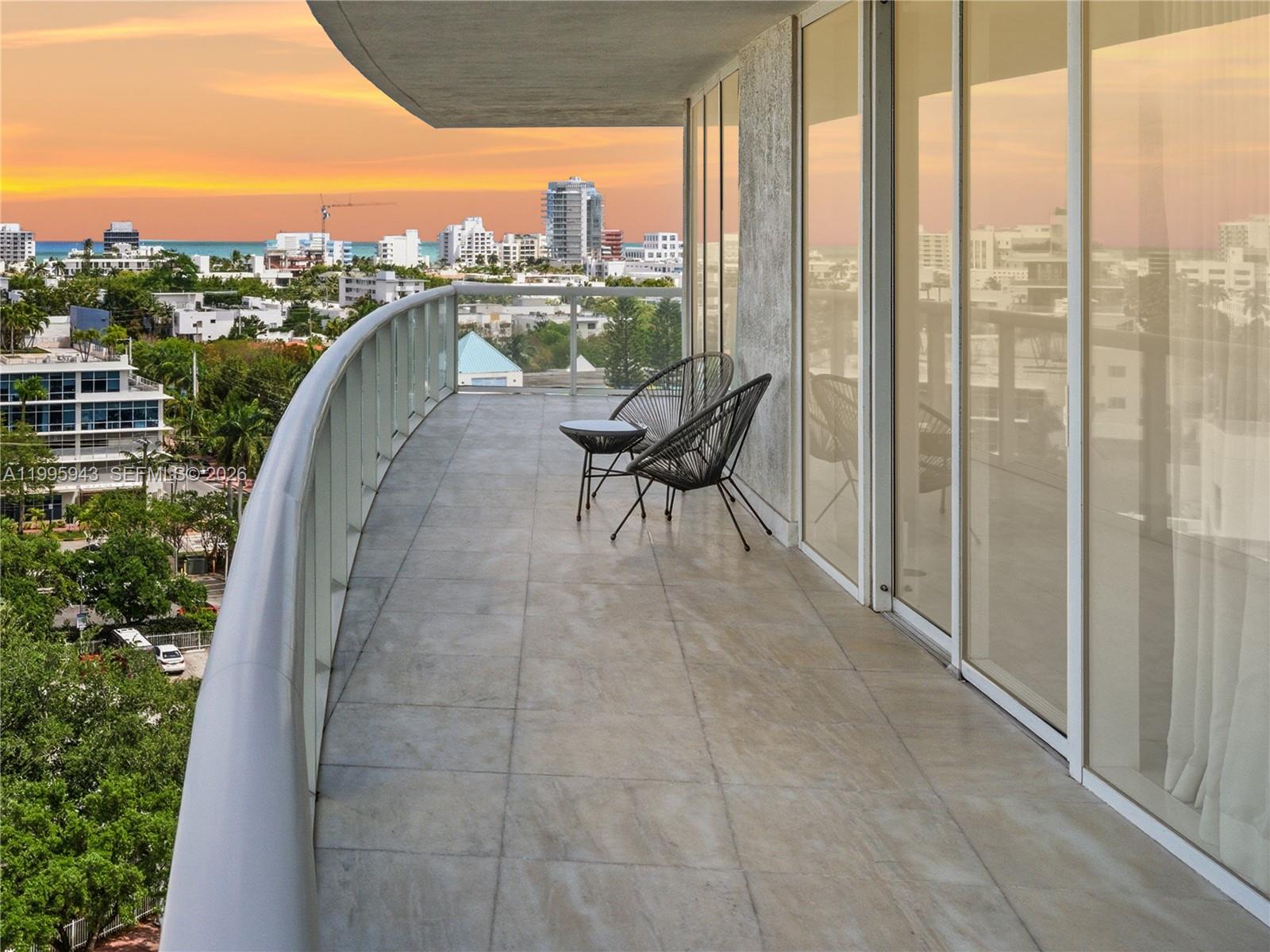 A balcony with tile flooring, two chairs, a small table, and a city skyline view — 450 Alton Rd # 910, Miami Beach FL 33139, MIAMI BEACH, FL