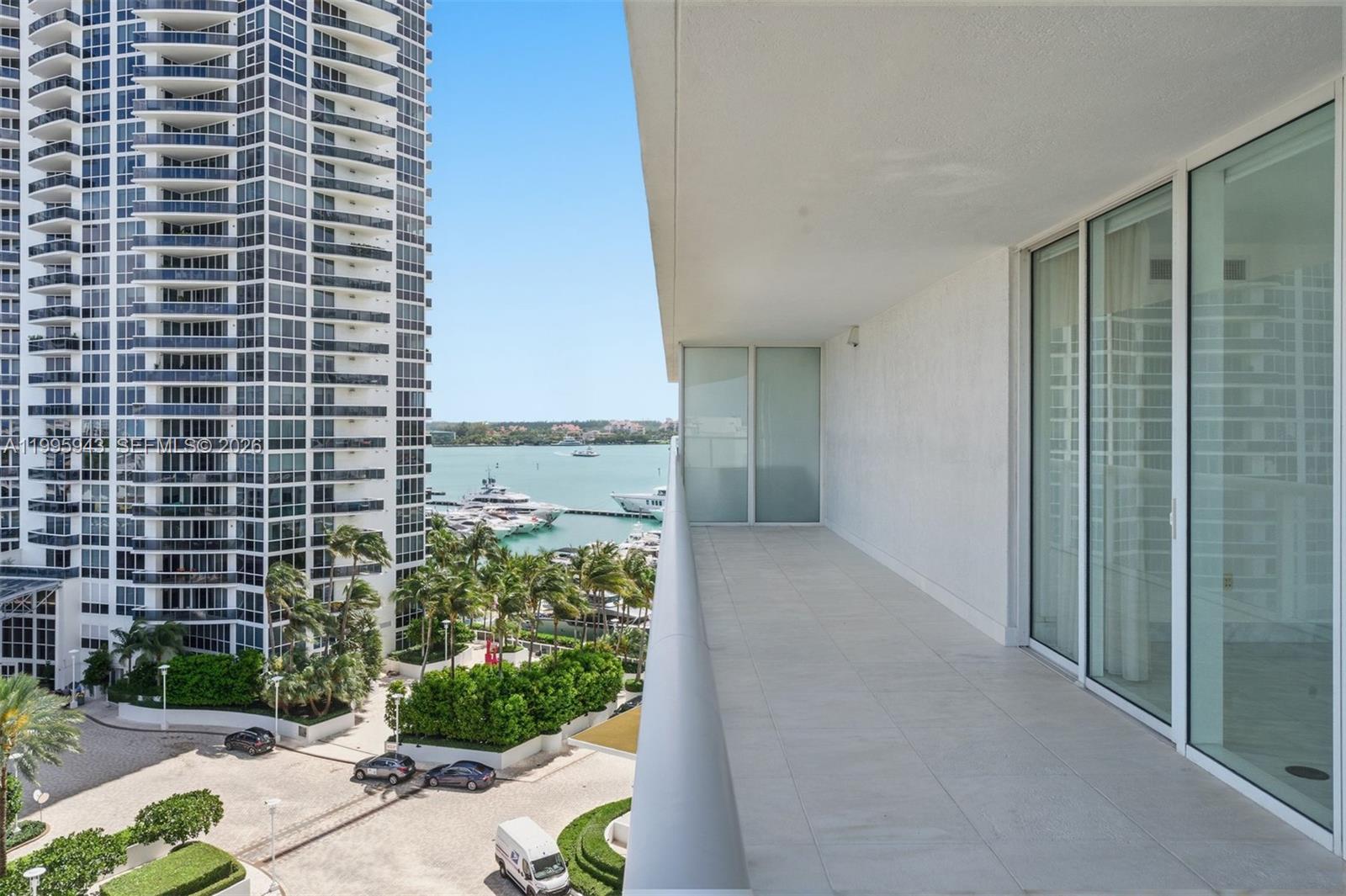 A balcony with light-colored tile flooring overlooks a marina, palm trees, and a tall building — 450 Alton Rd # 910, Miami Beach FL 33139, MIAMI BEACH, FL