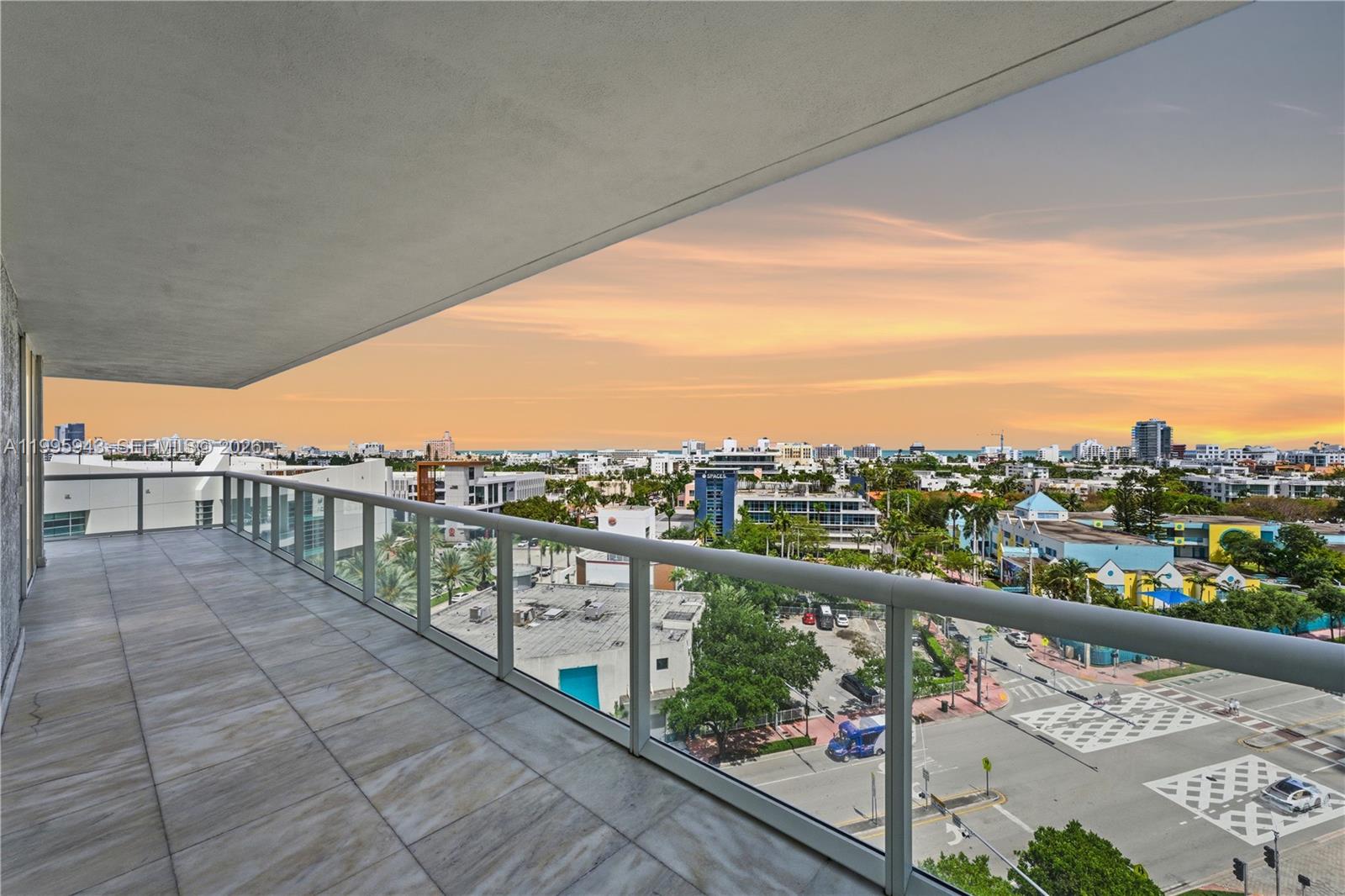 A high-rise balcony with glass railings overlooks a city street and the distant ocean — 450 Alton Rd # 910, Miami Beach FL 33139, MIAMI BEACH, FL