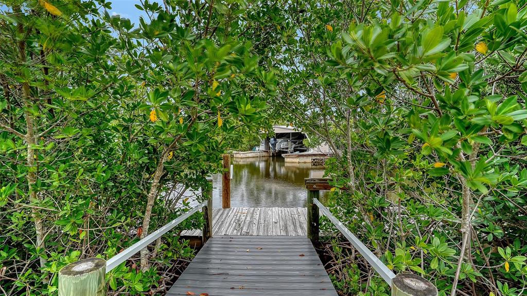A wooden dock leads through dense green mangroves toward a boat lift on the water — 4324 SALTWATER PEARL WAY, CORTEZ, FL