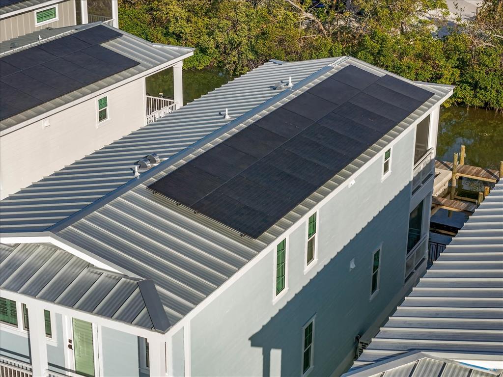 An aerial view shows the metal roofs of two adjacent houses with installed solar panels — 4324 SALTWATER PEARL WAY, CORTEZ, FL