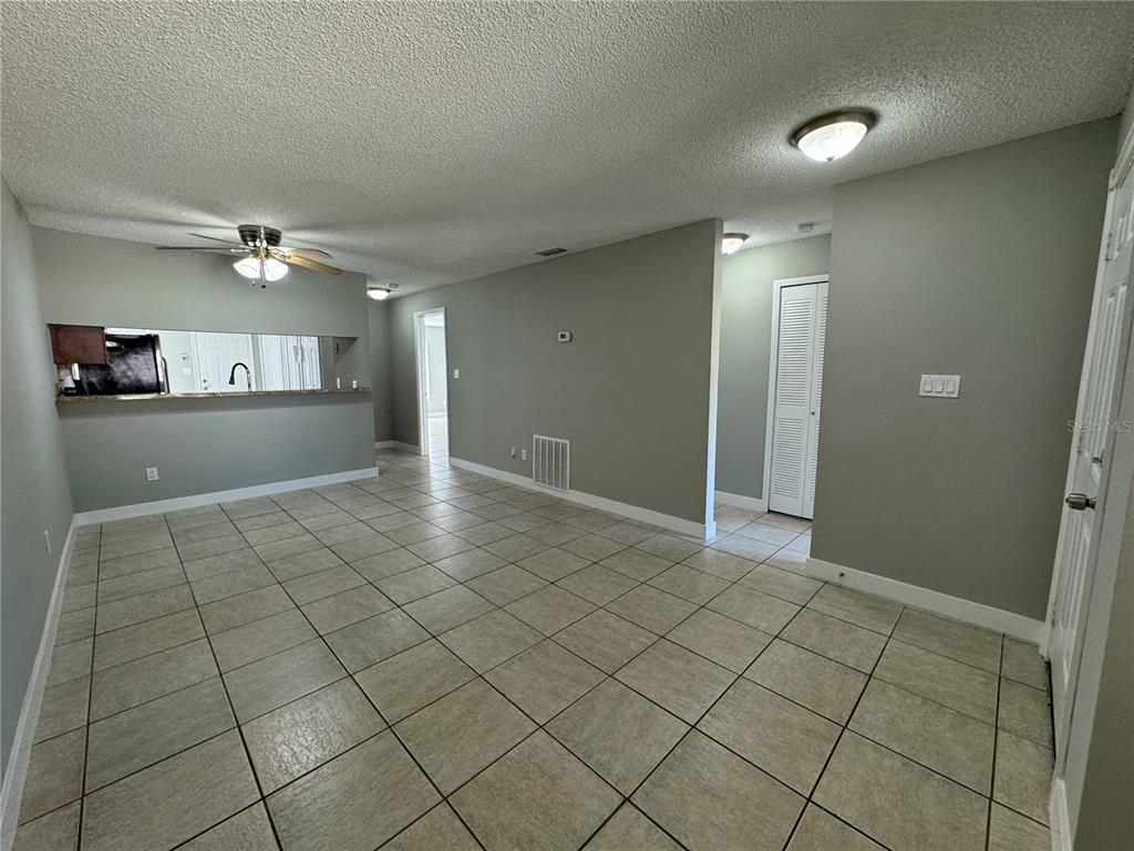 An open-concept living area with light gray walls, tiled flooring, and a kitchen pass-through window — 1357 SOPHIE BOULEVARD, ORLANDO, FL