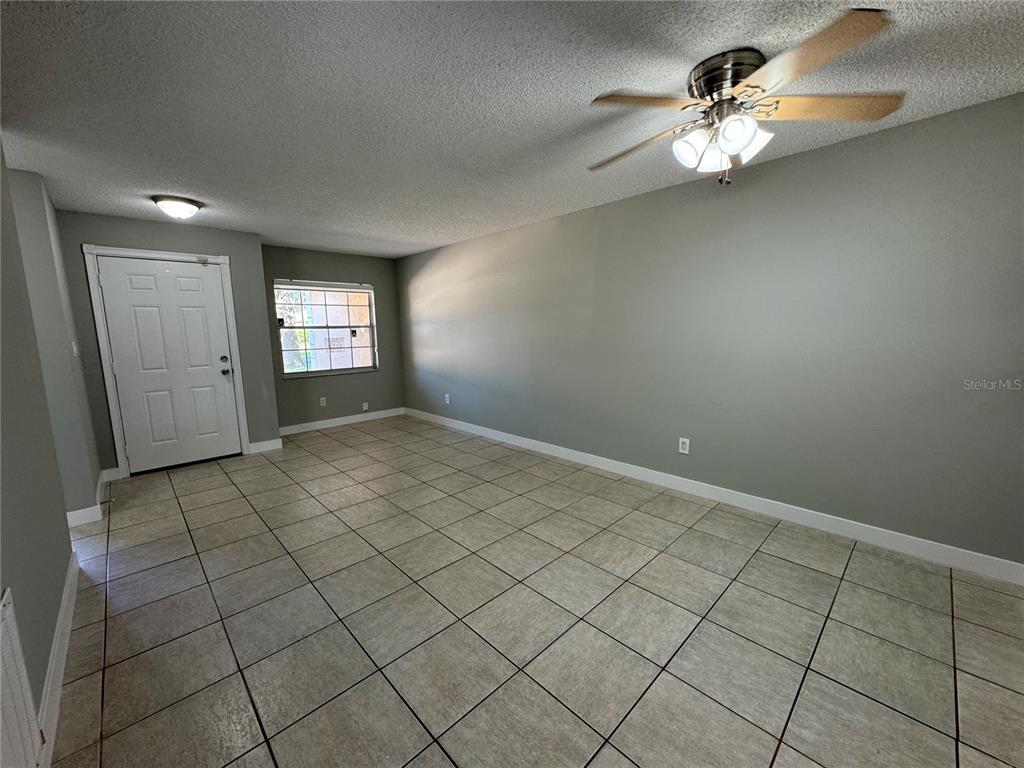 An empty room features light-colored tile flooring, gray walls, a ceiling fan, and a front door — 1357 SOPHIE BOULEVARD, ORLANDO, FL
