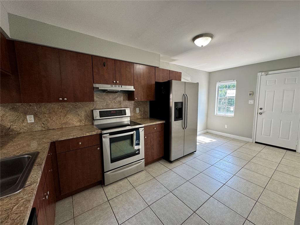A kitchen features dark wood cabinets, granite countertops, stainless steel appliances, and light tile flooring — 1357 SOPHIE BOULEVARD, ORLANDO, FL