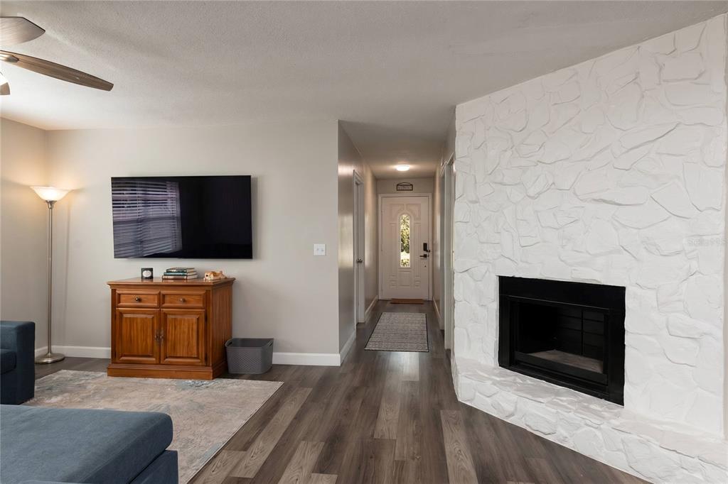 A living room features a white stone fireplace, wood-look flooring, and a hallway leading outside — 4703 SERENA DRIVE, TAMPA, FL