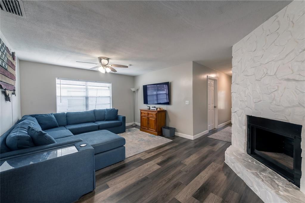 A living room features a blue sectional sofa, a fireplace with white stone, and wood-look flooring — 4703 SERENA DRIVE, TAMPA, FL