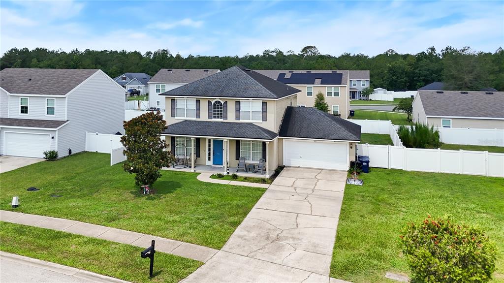 A two-story suburban house features a blue front door, a concrete driveway, and white fencing — 586 INDEPENDENCE DRIVE, MACCLENNY, FL