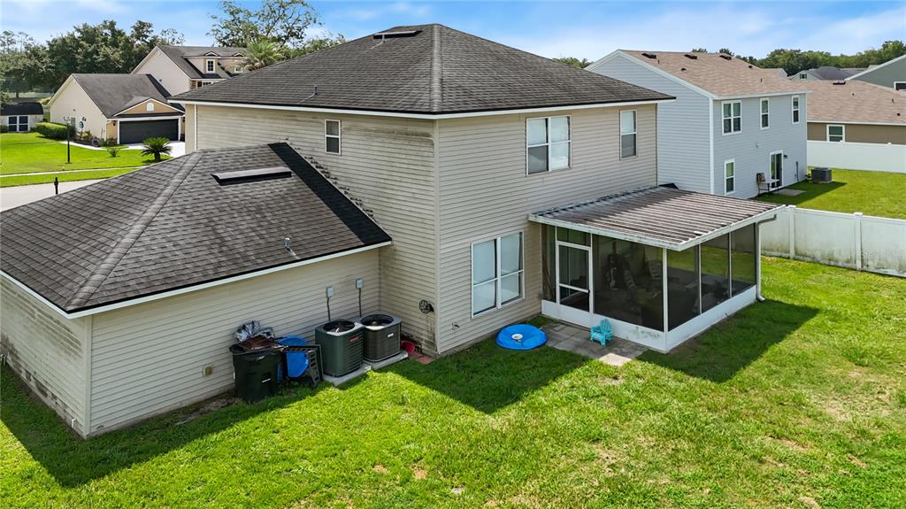 An exterior view of a two-story beige house with a screened-in patio and backyard — 586 INDEPENDENCE DRIVE, MACCLENNY, FL
