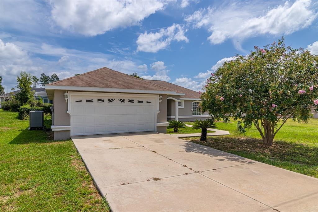 A single-story house with a beige exterior, a two-car garage, and a flowering tree — 14771 SW 27TH COURT ROAD, OCALA, FL