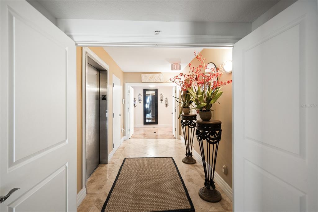 A tiled hallway features an elevator, decorative plant stands, and a framed mirror — 1350 GULF BOULEVARD UNIT 901, CLEARWATER BEACH, FL