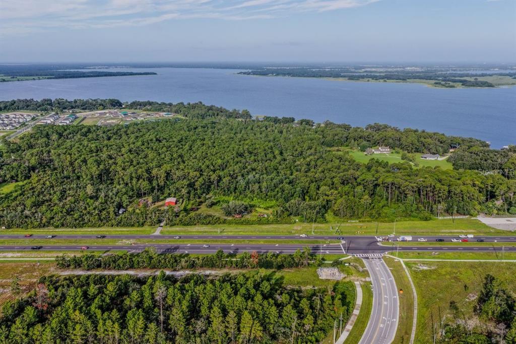 An aerial view shows a large wooded lot bordering a lake near a divided highway — 0 E IRLO BRONSON MEMORIAL HIGHWAY, ST CLOUD, FL