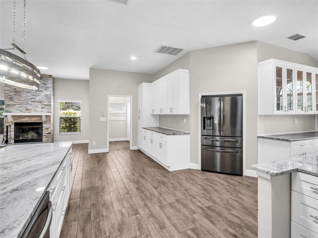 A kitchen features white cabinetry, granite countertops, stainless steel appliances, and wood-look tile flooring — 447 WHISPERING LAKES BOULEVARD, TARPON SPRINGS, FL