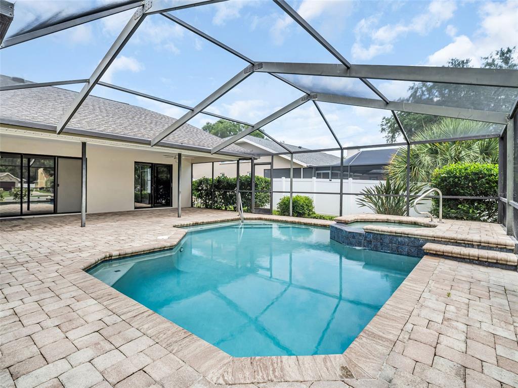A swimming pool and attached spa are enclosed within a screened lanai with paver decking — 447 WHISPERING LAKES BOULEVARD, TARPON SPRINGS, FL