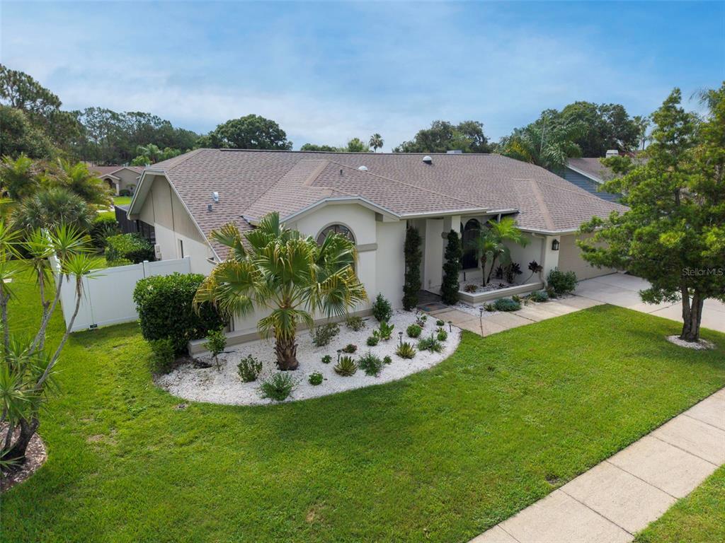 An exterior view of a single-story house with a white rock garden and palm tree — 447 WHISPERING LAKES BOULEVARD, TARPON SPRINGS, FL