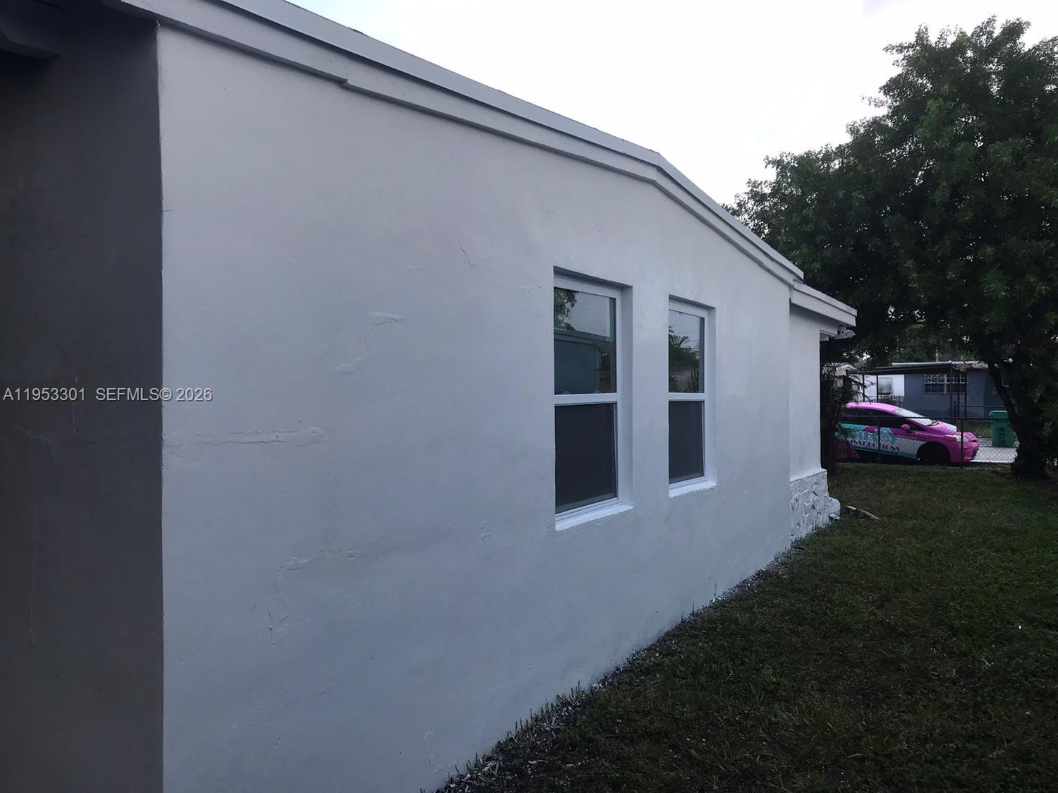 The exterior side wall of a white house features two windows and a grassy yard — 1920 Rutland St, Opa-Locka FL 33054, OPA-LOCKA, FL