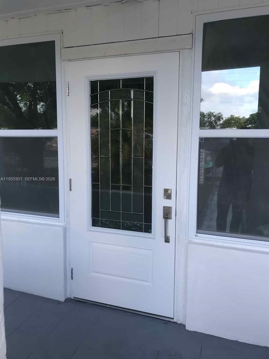 A white front door with a decorative glass insert is flanked by two large windows — 1920 Rutland St, Opa-Locka FL 33054, OPA-LOCKA, FL