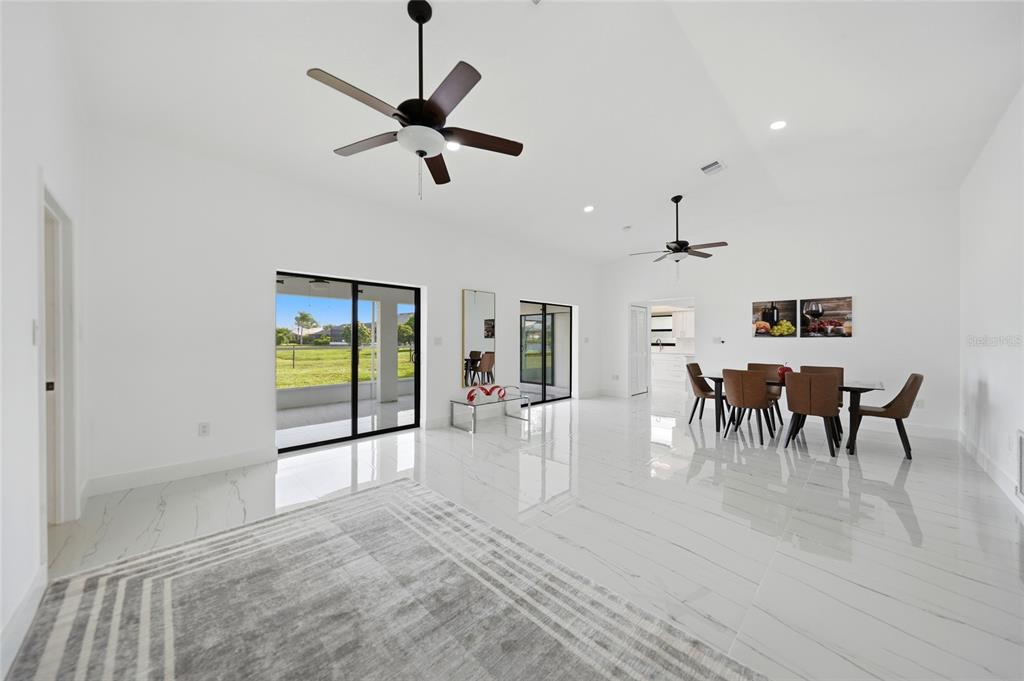 A bright, open-concept dining and living area features white marble floors, ceiling fans, and sliding doors — 2705 MAURITANIA ROAD, PUNTA GORDA, FL