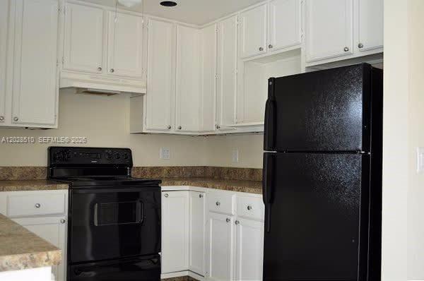 A kitchen features white cabinets, black appliances, and tan laminate countertops — FORT LAUDERDALE, FL