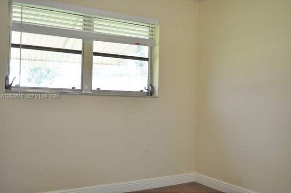 A corner of a room with beige walls, a window with white blinds, and carpeted flooring — FORT LAUDERDALE, FL