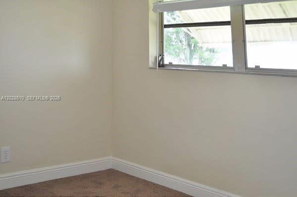 A corner of a room with beige walls, brown carpet, and a window with blinds — FORT LAUDERDALE, FL