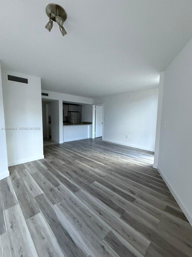 An empty room features light gray wood-look flooring and a view into a kitchen — 6955 NW 186th St # F209, Hialeah FL 33015, HIALEAH, FL