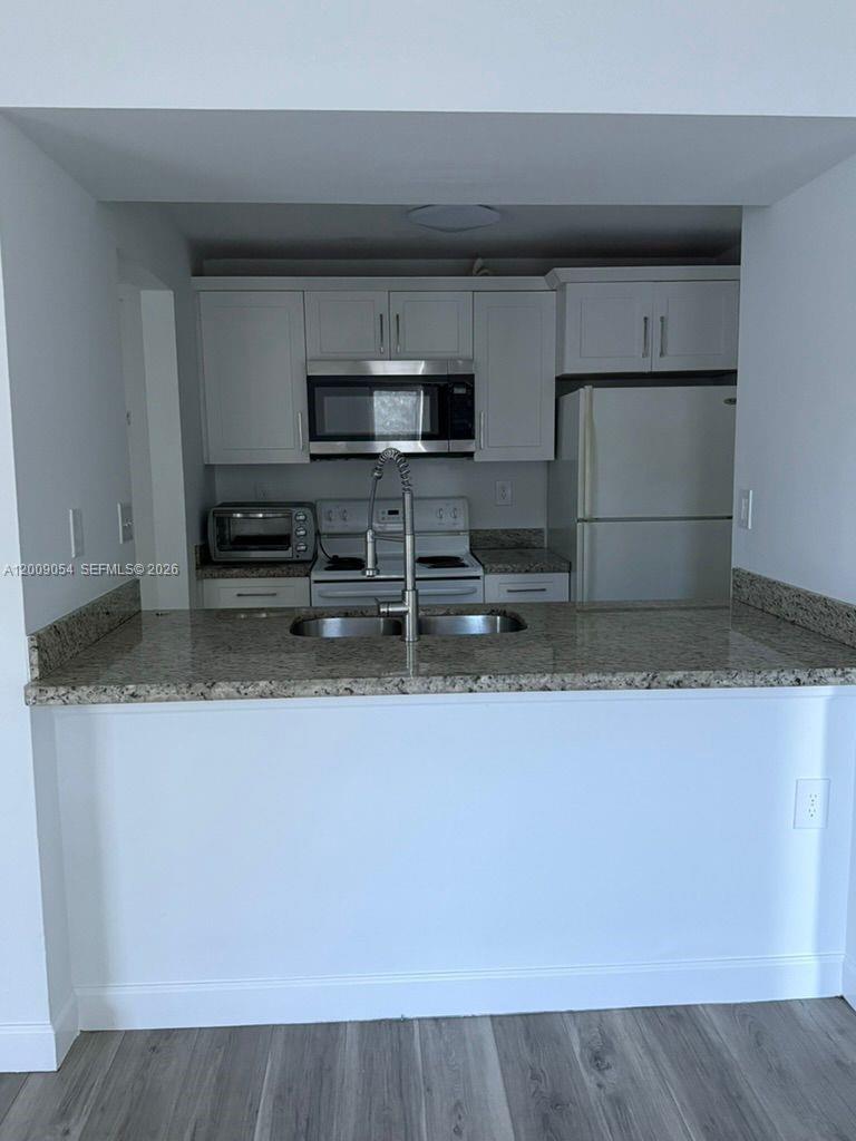 A kitchen features white cabinets, granite countertops, a stainless steel microwave, and a white refrigerator — 6955 NW 186th St # F209, Hialeah FL 33015, HIALEAH, FL