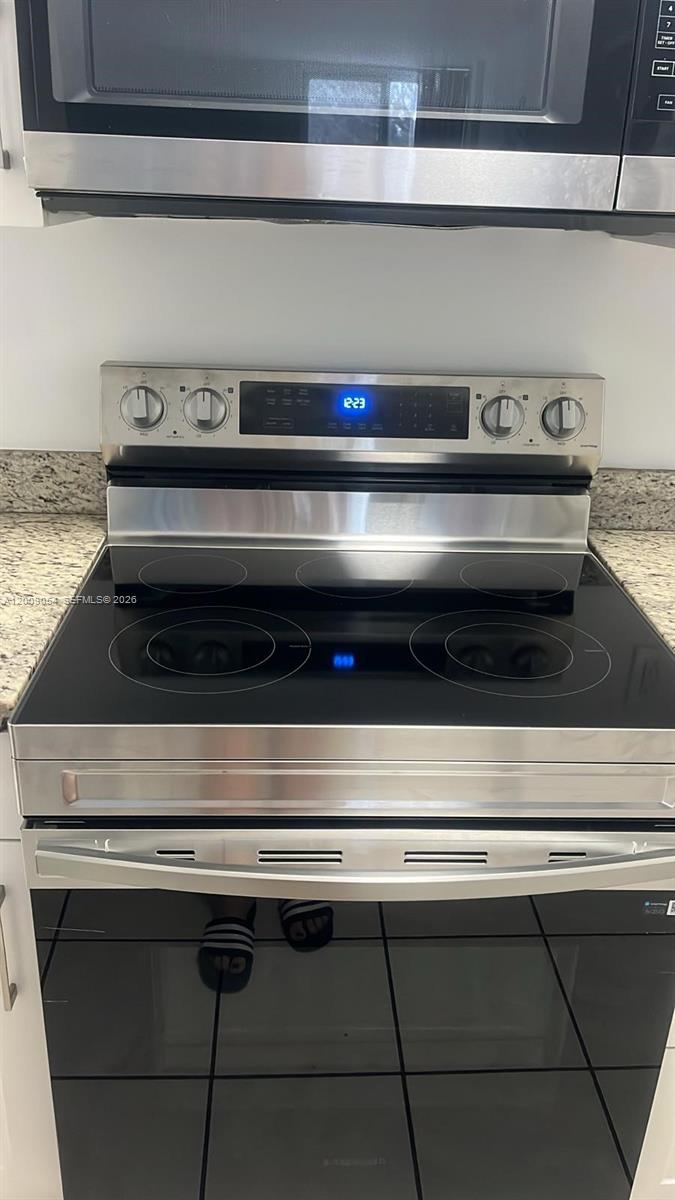 A stainless steel electric range with a glass cooktop is positioned below a microwave — 6955 NW 186th St # F209, Hialeah FL 33015, HIALEAH, FL