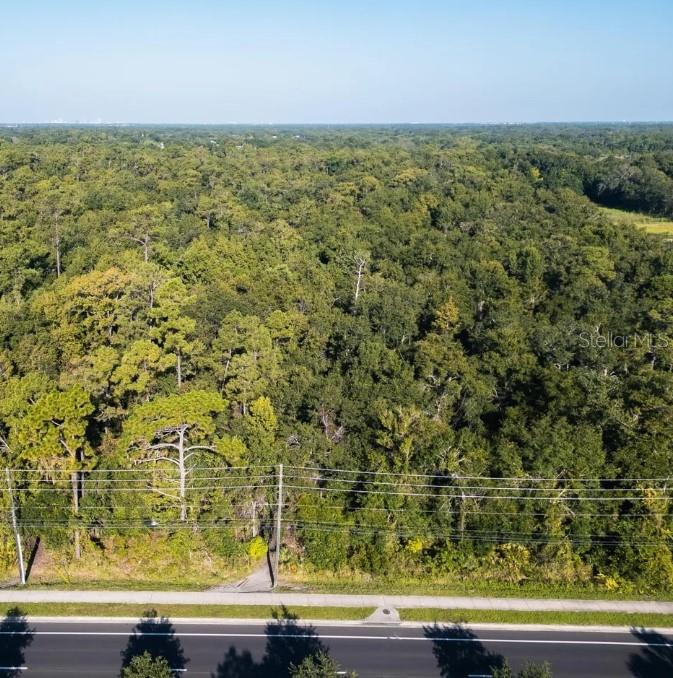 An aerial view shows a dense, wooded lot bordering a paved road and sidewalk — 2322-2328 ROUSE ROAD, ORLANDO, FL