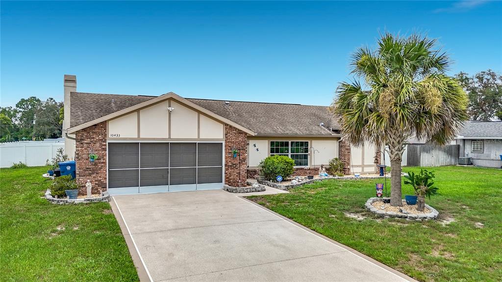 A single-story house with a brick facade, a screened garage, and a palm tree in front — 10433 DUNKIRK ROAD, SPRING HILL, FL