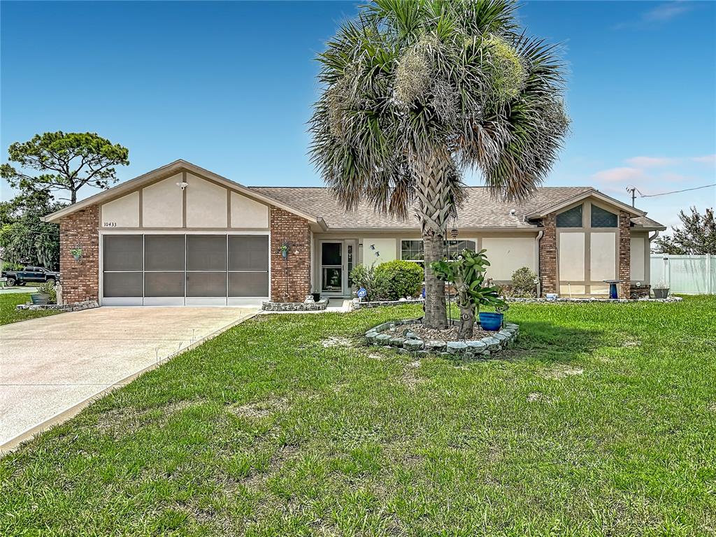 A single-story house with a screened garage, brick accents, and a large palm tree — 10433 DUNKIRK ROAD, SPRING HILL, FL