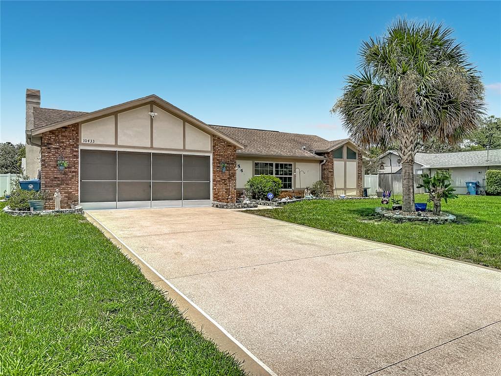 A single-story house with a brick facade, a screened garage, and a large palm tree — 10433 DUNKIRK ROAD, SPRING HILL, FL