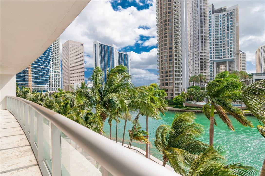 A balcony with a glass railing overlooks a canal, palm trees, and high-rise city buildings — 465 Brickell Avenue # 419, Miami FL 33131, MIAMI, FL