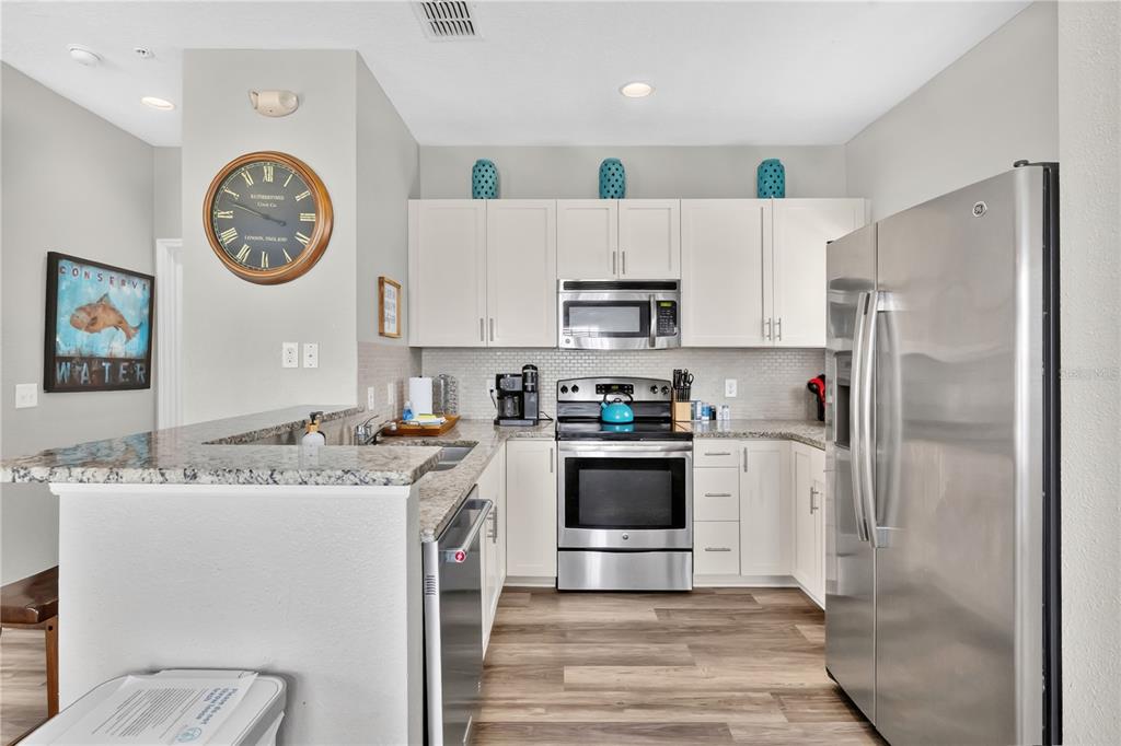 A kitchen features white cabinets, stainless steel appliances, granite countertops, and wood-look flooring — 5352 DIPLOMAT COURT UNIT 108, KISSIMMEE, FL