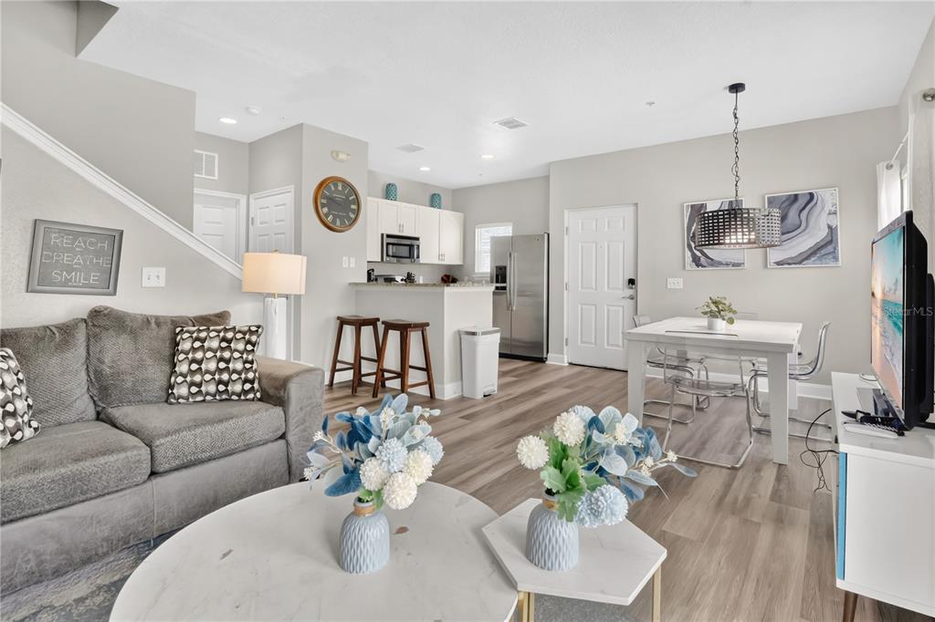 An open-concept living and dining area features light wood flooring, a gray sofa, and kitchen — 5352 DIPLOMAT COURT UNIT 108, KISSIMMEE, FL