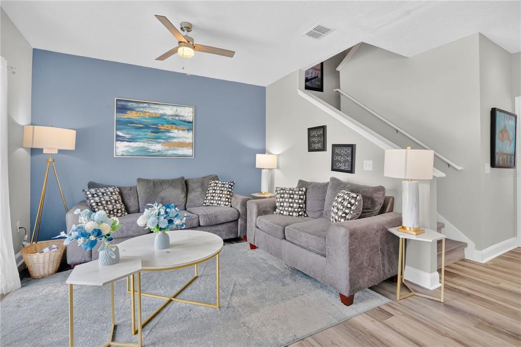 A living room features two gray sofas, a blue accent wall, and a staircase — 5352 DIPLOMAT COURT UNIT 108, KISSIMMEE, FL