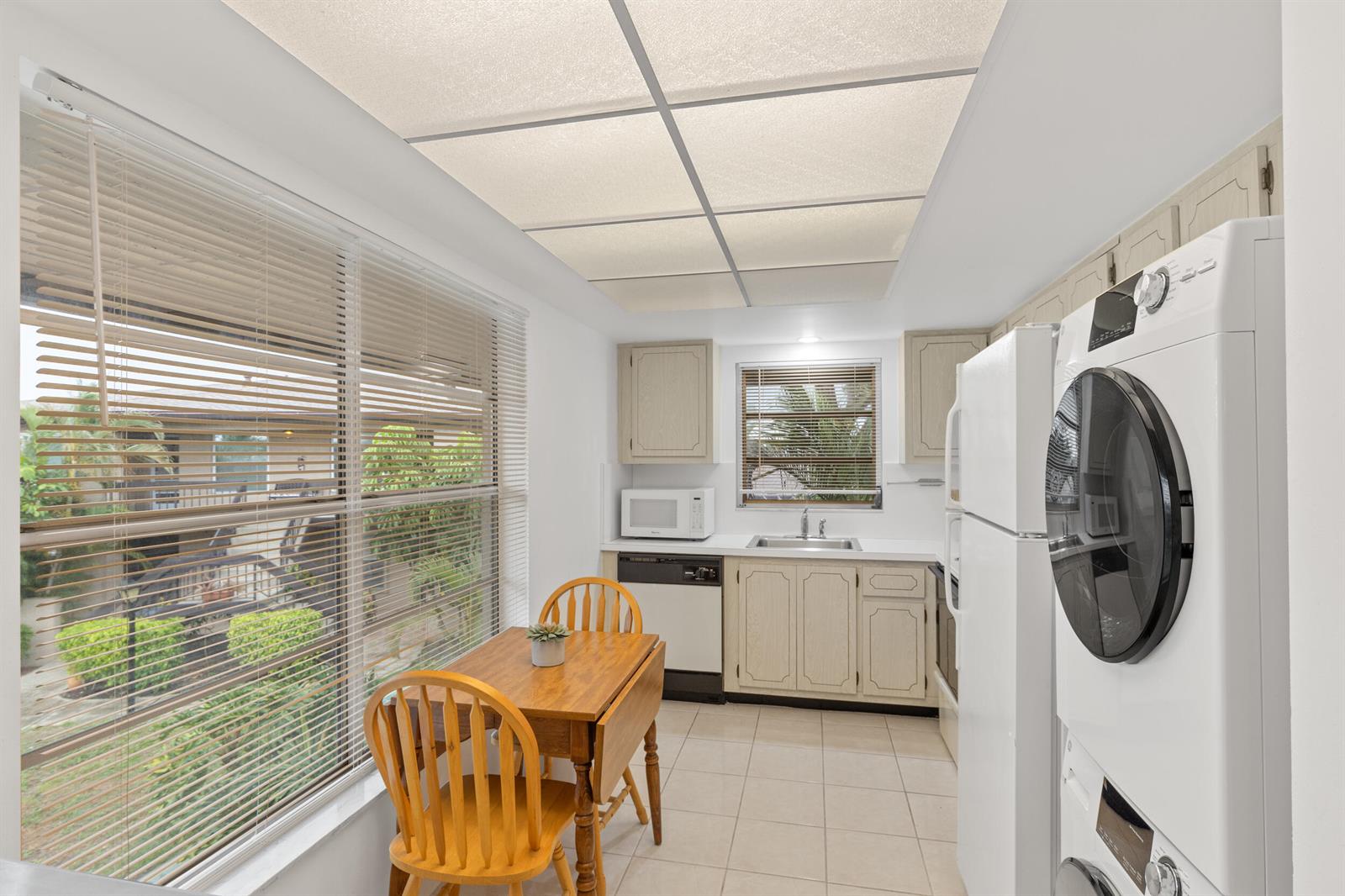 A kitchen with a small dining table, white appliances, a stacked washer-dryer, and large windows — 13623 Via Aurora # C, Delray Beach FL 33484, DELRAY BEACH, FL
