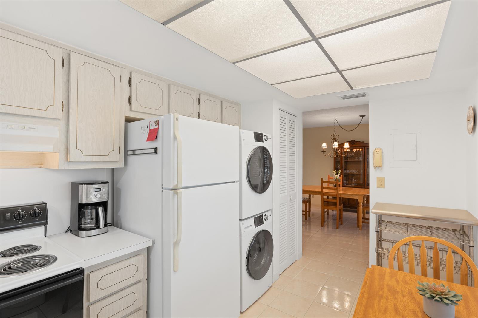 A kitchen with white cabinets, a refrigerator, stacked laundry units, and a view into a dining room — 13623 Via Aurora # C, Delray Beach FL 33484, DELRAY BEACH, FL