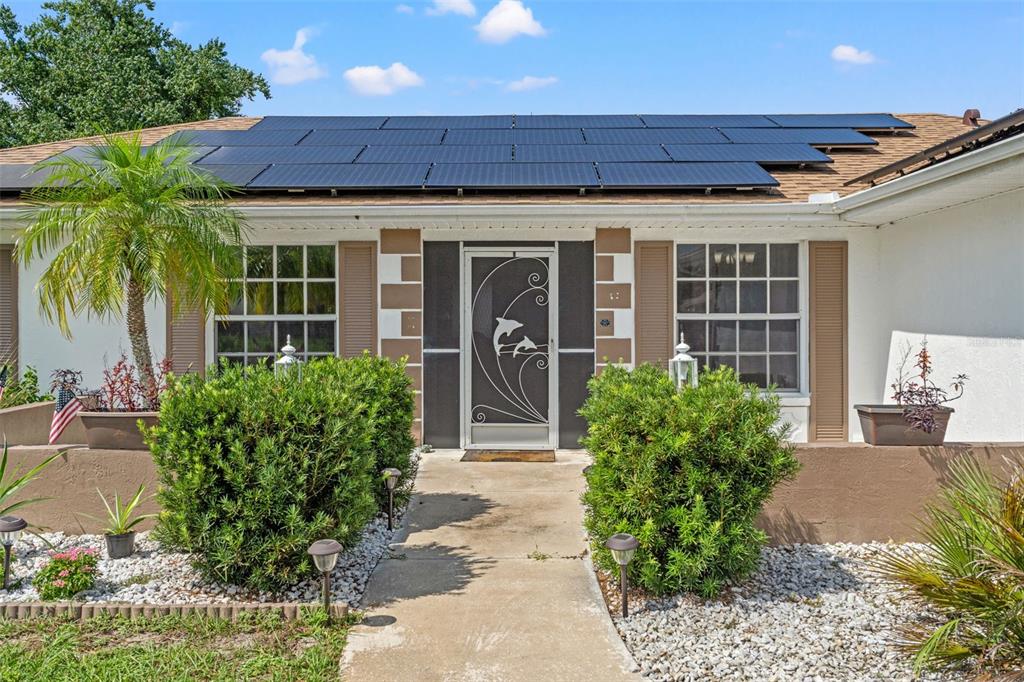 A single-story house exterior features a solar panel roof, a dolphin-patterned screen door, and landscaping — 3077 ARDENWOOD DRIVE, SPRING HILL, FL