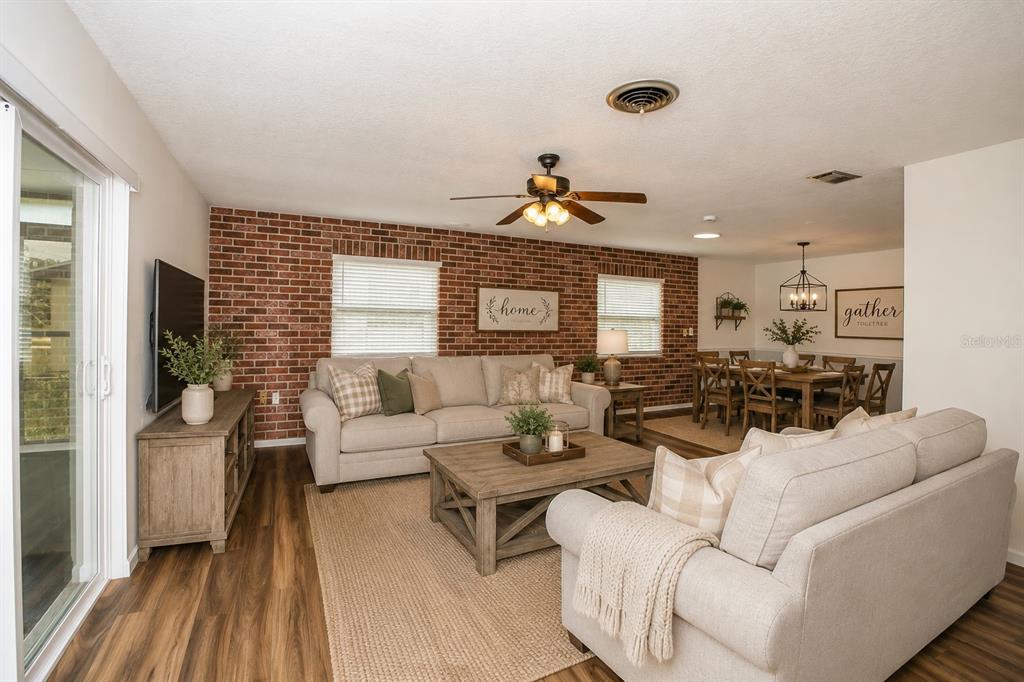 A living room and dining area featuring a brick accent wall and neutral furniture — 3019 TAMPICO DRIVE, ORLANDO, FL