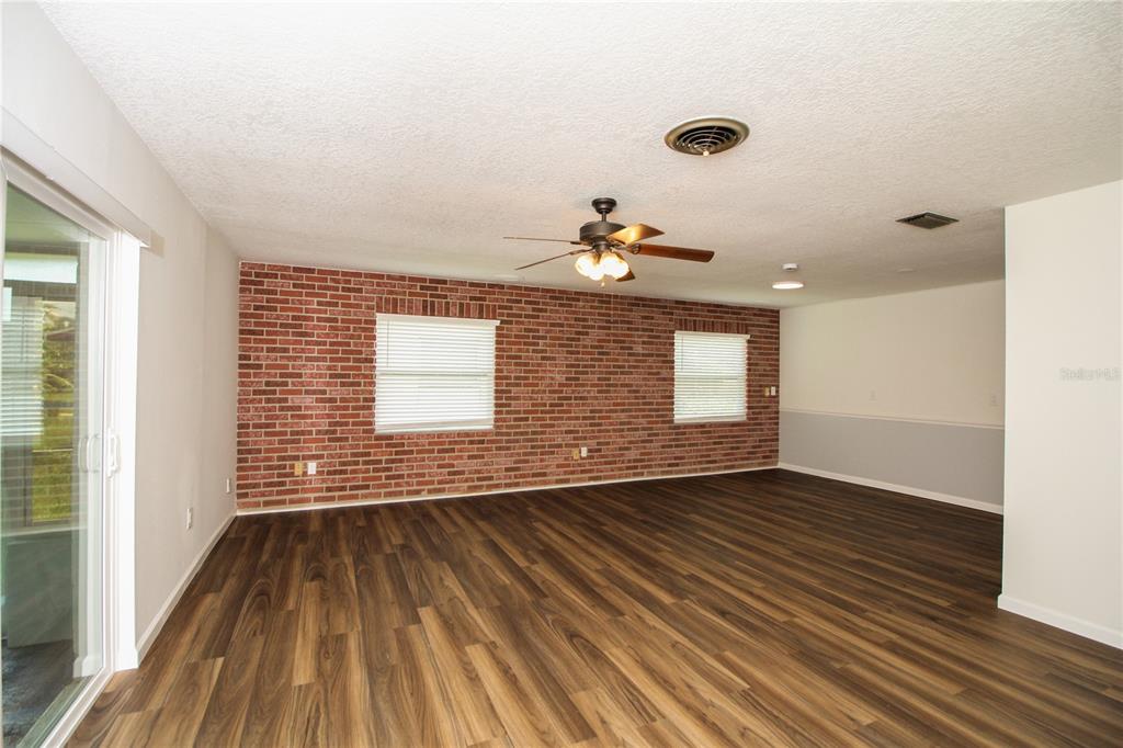 An empty living room features a brick accent wall, wood-look flooring, and a ceiling fan — 3019 TAMPICO DRIVE, ORLANDO, FL