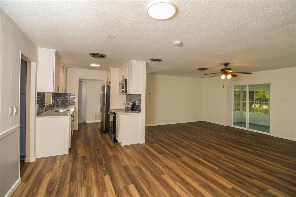 An open-concept kitchen and living area feature wood-look flooring, white cabinetry, and sliding glass doors — 3019 TAMPICO DRIVE, ORLANDO, FL