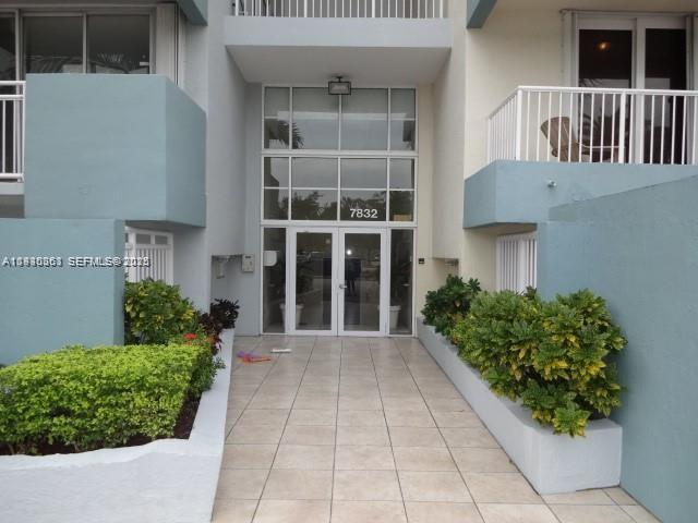 The exterior entrance of a building features a glass door, tiled walkway, and landscaped planters — 7832 Collins Ave # 403, Miami Beach FL 33141, MIAMI BEACH, FL