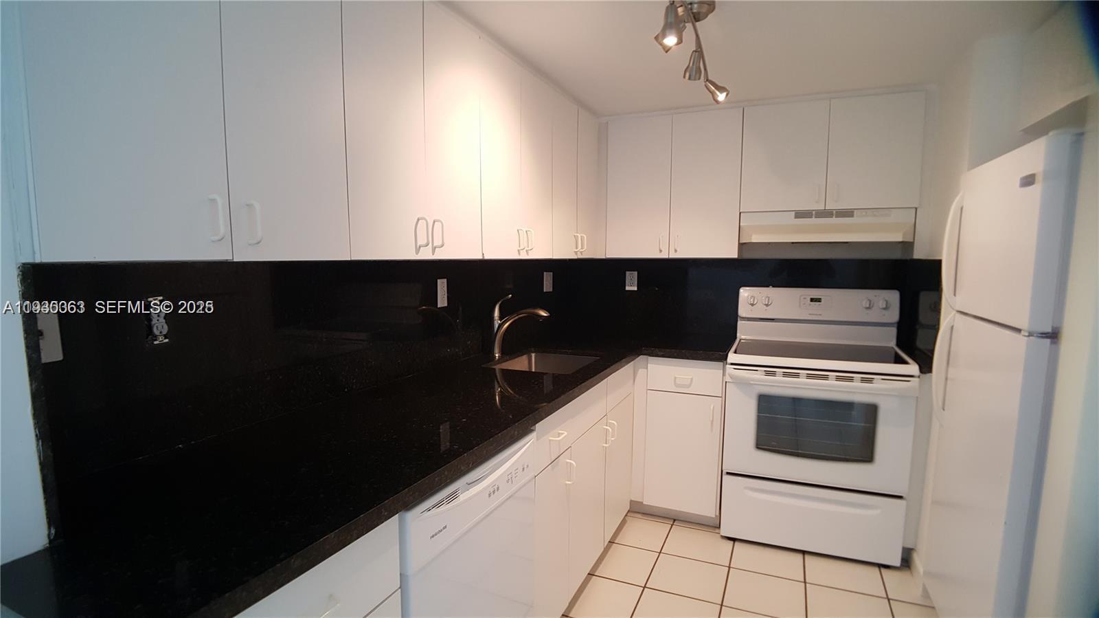 A kitchen features white cabinets, black countertops, white appliances, and light-colored floor tiles — 7832 Collins Ave # 403, Miami Beach FL 33141, MIAMI BEACH, FL