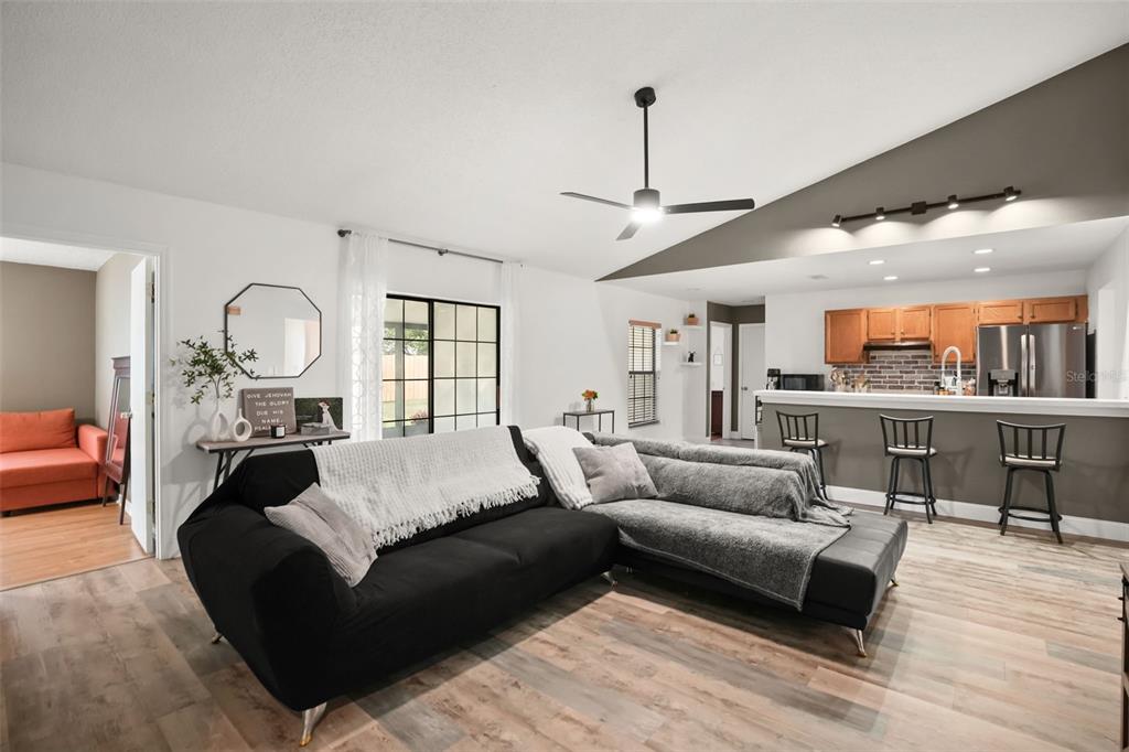 A living room with a black sectional sofa, vaulted ceiling, and an open kitchen beyond — 4613 FLATWOOD LANE, ORLANDO, FL